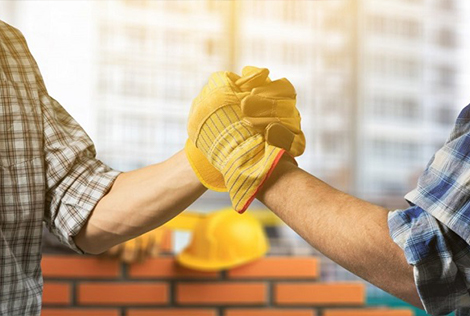 2 Photographie de deux bras d'ouvriers qui se serrent la main avec leur gants sur fond de chantier en arrière plan pour évoquer le recrutement dans le BTP