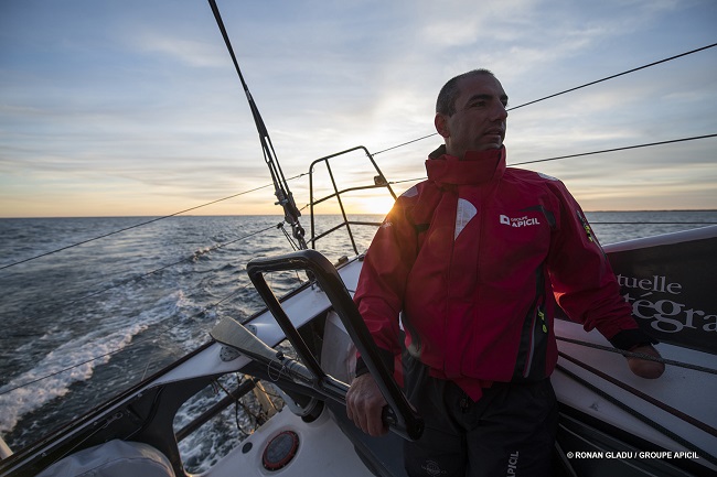 Damien Seguin qui tient la barre de son bateau en plein couché de soleil à l'horizon du Vendee globe