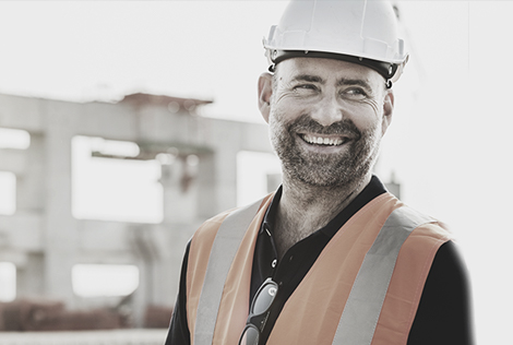 2 Un ouvrier sur un chantier avec son casque et son gilet souriant pour évoquer la couverture du mag reglementaire MBTP