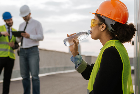 2 Photographie d'une femme sur un chantier avec son casque qui se désaltère pour éviter les risques canicule et fortes chaleurs