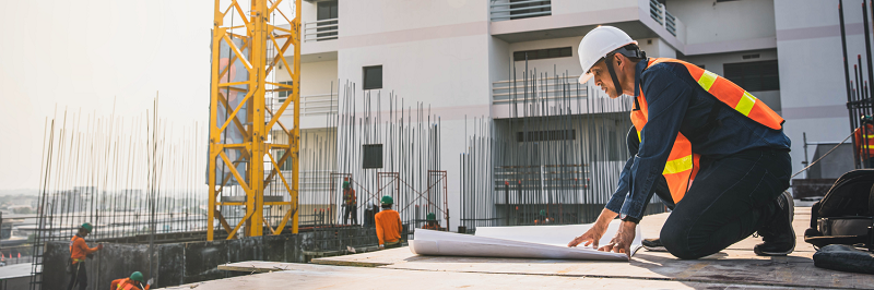 Un ouvrier à genou sur le bord d'un immeuble en chantier regarde un plan dans le cadre de l'offre collective de prévoyance des professionnels du BTP