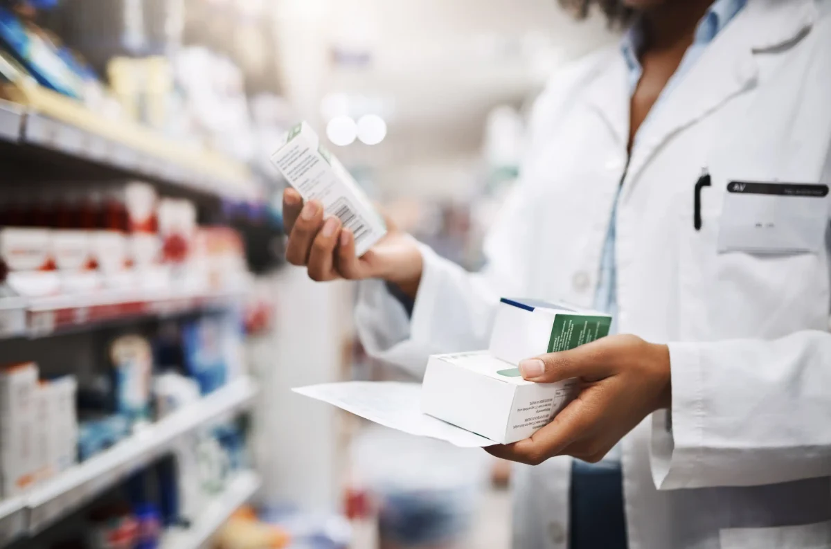 Professionnel de santé tenant plusieurs boîtes de médicaments dans une pharmacie, illustrant les nouvelles règles de remboursement des médicaments biosimilaires et hybrides.